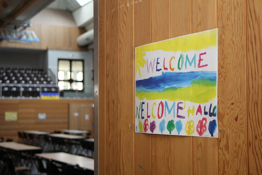 Blick in eine zur Notunterkunft eingerichtete Halle, im Vordergrund ein Bild "Welcome"