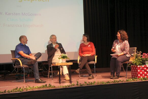 Auf dem Podium: Dr. Karsten McGovern, ehemaliger Erster Kreisbeigeordneter des Landkreises Marburg-Biedenkopf (v.l.), Claus Schäfer, ehemaliger Leiter des Büros für Integration (BfI), Dr. Franziska Engelhardt, Leiterin des BfI und die Moderatorin der Veranstaltung, Simona Lison