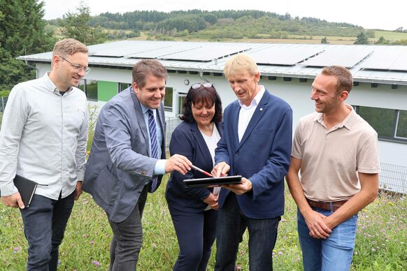 Gerrit Schönberger (Fachdienstleiter „Technisches Gebäudemanagement“, Landkreis), der Erste Kreisbeigeordnete und Schuldezernent Marian Zachow, Tatjana Ruppert (Schulleiterin Berglandschule Bad Endbach), Reiner Röder (Fachbereichsleiter „Schule und Gebäudemanagement“, Landkreis) und Jan Willems (Konrektor an der Berglandschule) im Austausch. Im Hintergrund ist eines der Solardächer an der Berglandschule in Bad Endbach zu sehen.